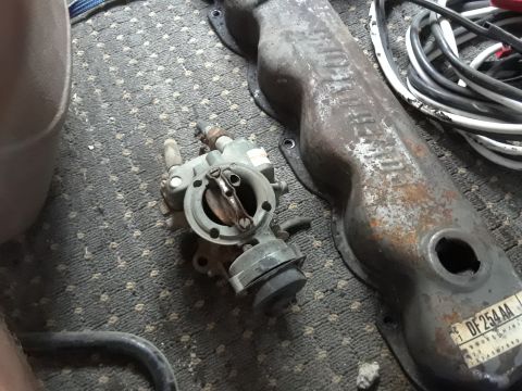 1994 Ford Bronco - A carburetor and a rusty valve cover with a "DF254AA" sticker are on a carpeted surface.