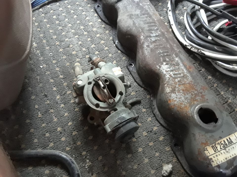 Carburetor and a rusty valve cover with sticker on carpet