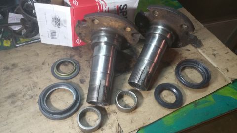 1996 Ford Bronco - Two metal spindle assemblies and several bearing seals are laid out on a workbench. A red and white box with the DANA logo is visible in th…