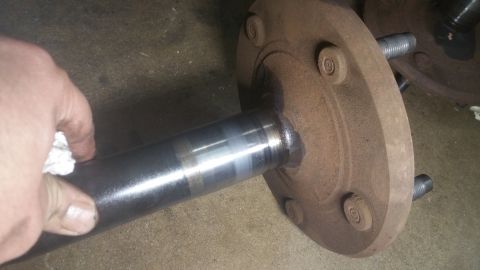 1996 Ford Bronco - A hand with a white rag is cleaning a metal axle shaft that is attached to a rusty brake drum assembly. The axle shaft has a shiny, polishe…