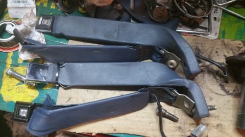 1996 Ford Bronco - Three blue seatbelt assemblies are laid out on a work surface. Each assembly features a metal buckle and a plastic housing with a bolt atta…