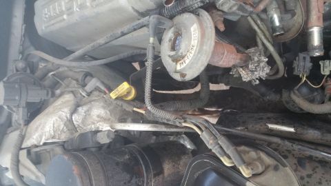 1996 Ford Bronco - A close-up view of the engine bay of a 1996 Ford Bronco, showing various engine components, hoses, and wiring harnesses. A yellow tag readi…