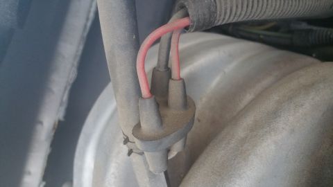 1996 Ford Bronco - Close-up view of two red wires connected to a black distributor cap with a ribbed black hose above. The components appear dusty and are mou…