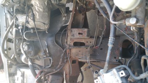 1996 Ford Bronco - The image shows a close-up view of the engine bay of a 1996 Ford Bronco, focusing on the rusted frame and various engine components. Hoses,…