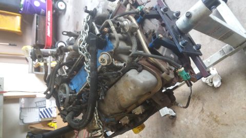 1996 Ford Bronco - A disassembled engine, likely from a Ford Bronco, is mounted on an engine stand. The engine is covered in various hoses, wires, and a metal…