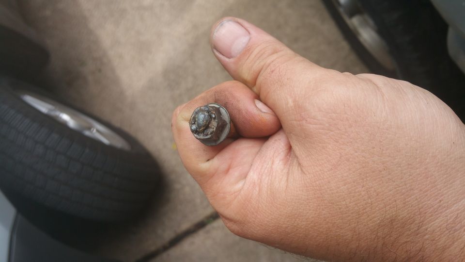 Hand holding a lug nut with a tire and wheel in the background.