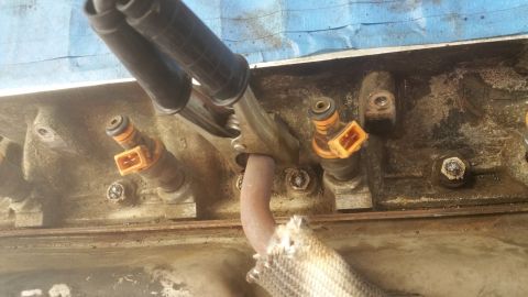 1996 Ford Bronco - A close-up view shows several fuel injectors installed in a dirty engine block. A metal clamp is attached to a pipe near the injectors.