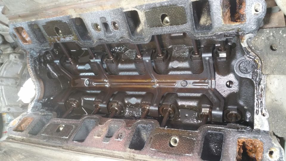 Overhead view of engine cylinder head with valve train components covered in oil.