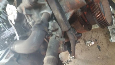 1996 Ford Bronco - A close-up view of a dirty engine component, likely part of a cooling system, with a metal pulley visible in the background. A chain is att…