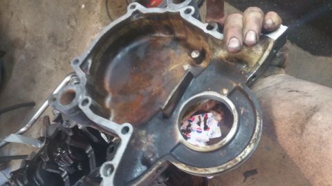 1996 Ford Bronco - A heavily rusted and greasy engine timing cover is held by a person's hands. The cover has a large circular opening in the center, with a p…
