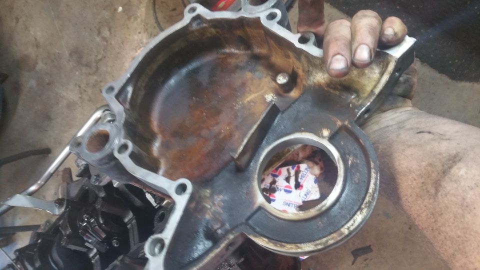 Rusted engine timing cover with paper inside, held by hands.