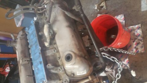 1996 Ford Bronco - An engine block with a silver valve cover is partially visible, along with blue protective material and a red bucket. A metal chain is drap…