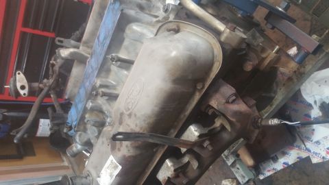 1996 Ford Bronco - A close-up view of a Ford V8 engine block with the valve cover removed, showing internal components and attached exhaust manifold with an o…