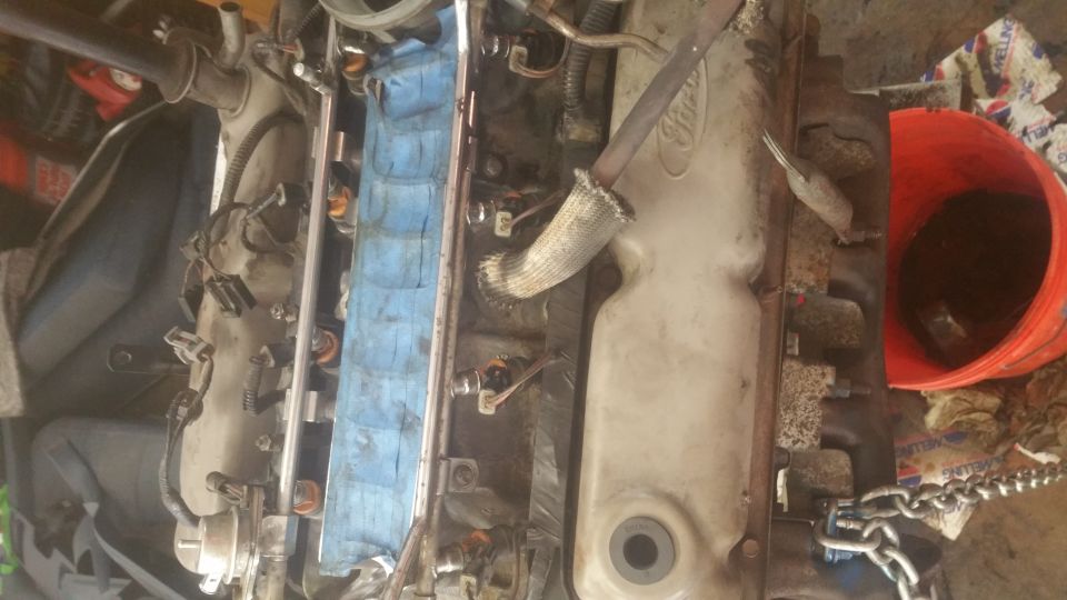 Overhead view of a Ford engine with fuel injectors, chain, and orange bucket.