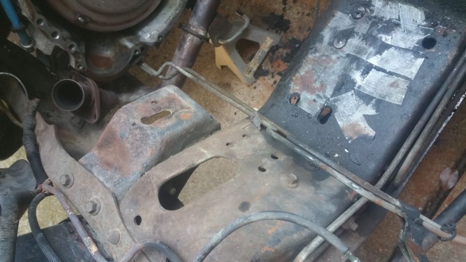 Rusty vehicle undercarriage with engine, exhaust, and frame components visible.