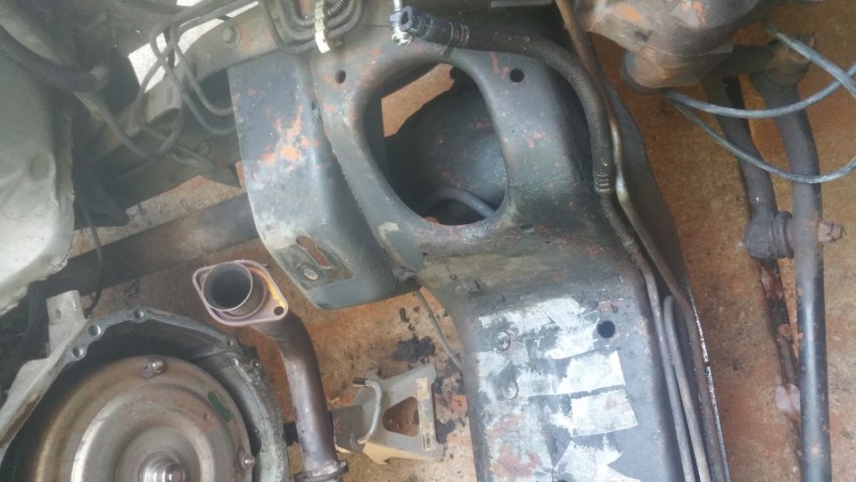Underside of a vehicle showing transmission, exhaust, and frame with rust and grime.