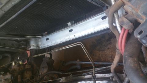 1996 Ford Bronco - This image shows a close-up view of the front of a vehicle, focusing on the radiator support bracket and surrounding engine components. The…