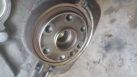 1996 Ford Bronco - A close-up view of a metal engine component, likely a crankshaft seal housing, with visible bolt holes and some stamped text on the outer r…