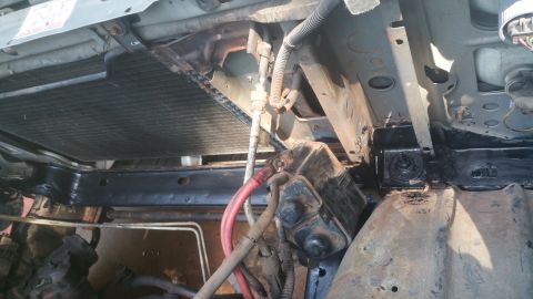 1996 Ford Bronco - Underneath the front of a 1996 Ford Bronco, the radiator and part of the engine bay are visible. A black painted frame rail and a battery a…