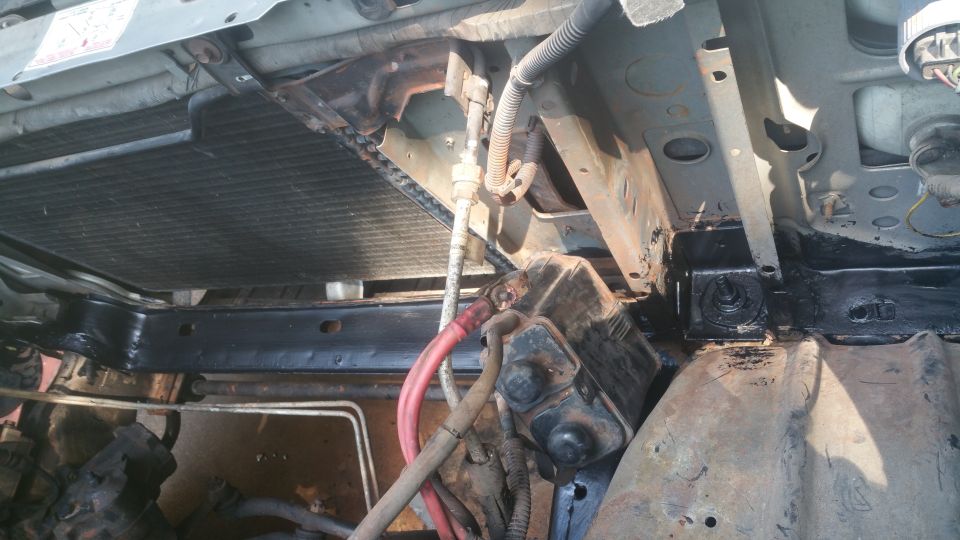 1996 Ford Bronco radiator and engine bay with black frame rail and battery.