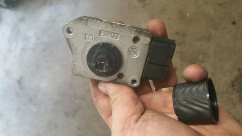 1996 Ford Bronco - A person holds a silver and black mass airflow sensor with the NGK logo visible. A ribbed black cap is held separately.