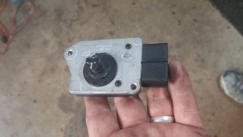 1996 Ford Bronco - A hand holds a silver mass air flow sensor with a black connector. The sensor has "NGK" and "F3" visible on its metal casing.