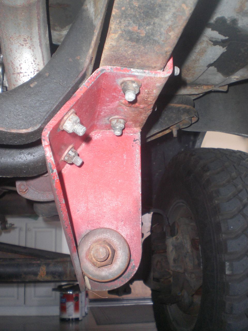 Underside view of a red bracket on a rusty leaf spring with bolts and a large washer.