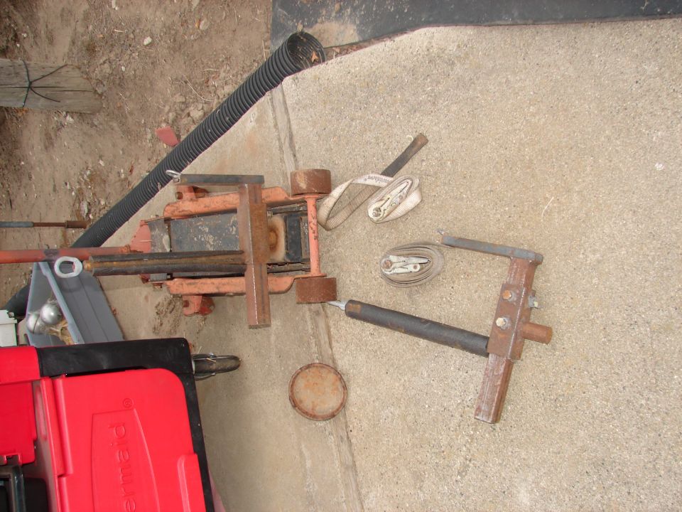 Tools and equipment including a hydraulic jack, straps, and a red toolbox on concrete.