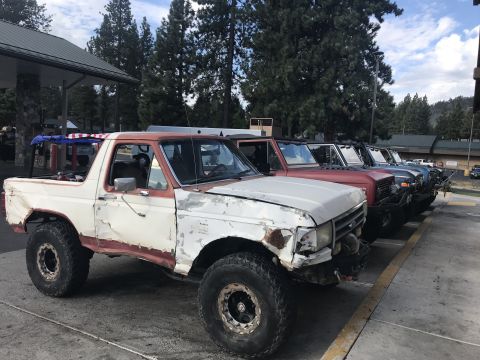 1984 Ford Bronco - A line of modified Ford Broncos are parked at a gas station. The lead Bronco is white with red accents and appears to be a convertible mode…