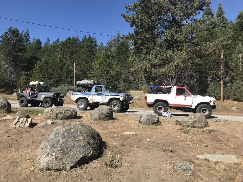 Three off-road vehicles parked on a dirt road with trees in the background.