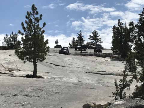 1984 Ford Bronco - Several off-road vehicles are parked on a large granite slab with scattered pine trees under a partly cloudy sky. One white Jeep Wrangler i…
