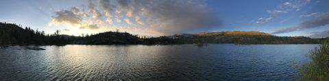 1984 Ford Bronco - A panoramic view of a calm lake surrounded by trees and hills under a dramatic sky with clouds illuminated by the setting sun.
