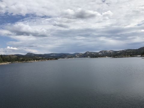 1984 Ford Bronco - A wide shot of a large, calm lake surrounded by forested hills and mountains under a cloudy sky.