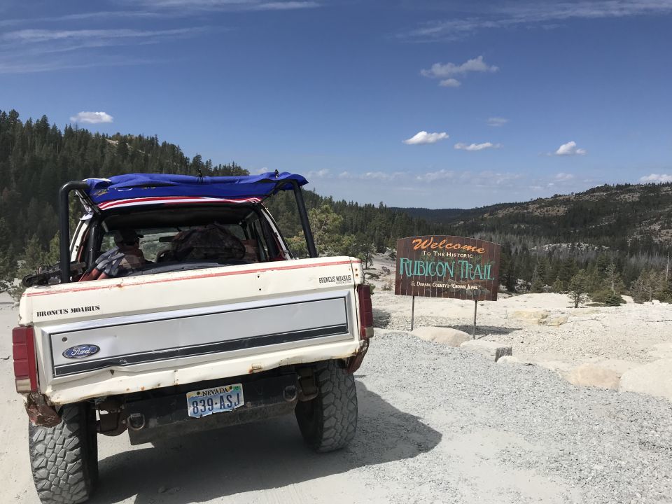 White 1980s Ford Bronco parked on dirt road by Rubicon Trail sign