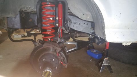 1996 Ford Bronco - The front suspension of a vehicle is shown, supported by jack stands. Visible components include a red coil spring, a red shock absorber, a…