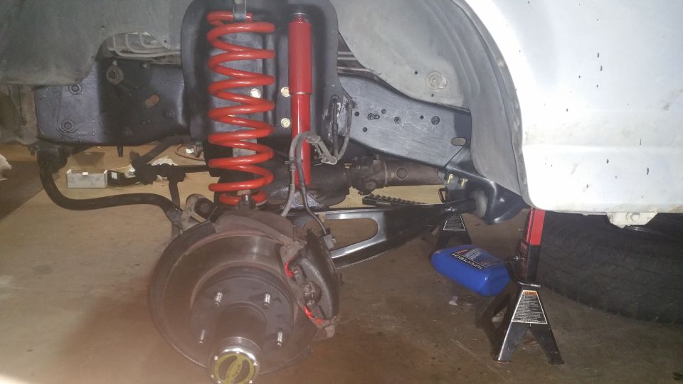 Front suspension of a vehicle with red coil spring and shock absorber, supported by jack stands.