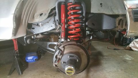 1996 Ford Bronco - The front suspension of a vehicle is shown, with a red coil spring and shock absorber prominently visible. A jack stand supports the vehicl…