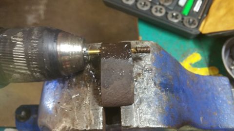 1996 Ford Bronco - A close-up view shows a drill chuck holding a small brass rod, which is being used to tap threads into a dark metal block. The block is sec…