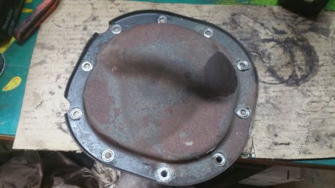 1996 Ford Bronco - A rusty differential cover with 12 bolts is shown on a workbench. A red and black tool handle is visible in the upper left corner.