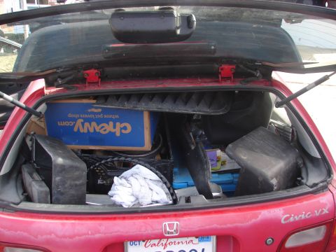1973 Ford Ranchero - The open trunk of a red hatchback is filled with various items, including a blue Chewy.com box, black plastic containers, and a pile of whi…
