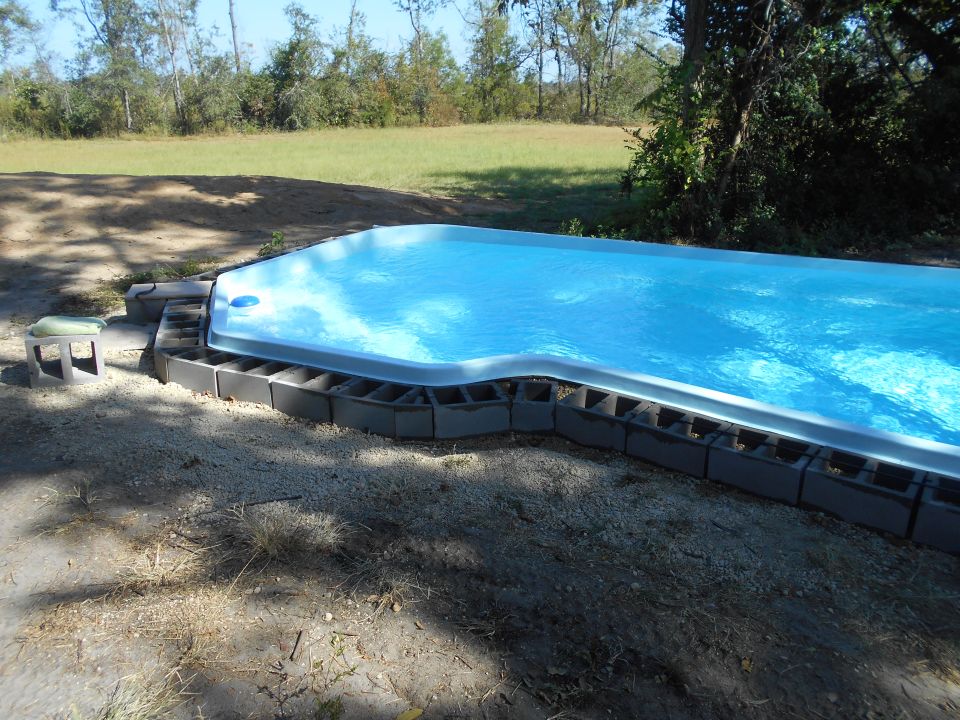 Above-ground swimming pool surrounded by cinder blocks, filled with blue water.