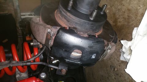 1996 Ford Bronco - A close-up view of a newly painted black brake caliper assembly on a vehicle, with a red coil spring visible in the foreground. The brake r…