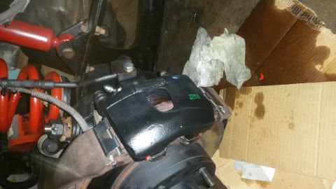 1996 Ford Bronco - A close-up view of a newly painted black brake caliper assembly on a vehicle's rear axle. The assembly is mounted near a red coil spring an…