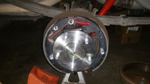 1996 Ford Bronco - A close-up view of a newly installed brake drum assembly on the rear axle of a vehicle, supported by a jack stand. The brake shoes, springs…