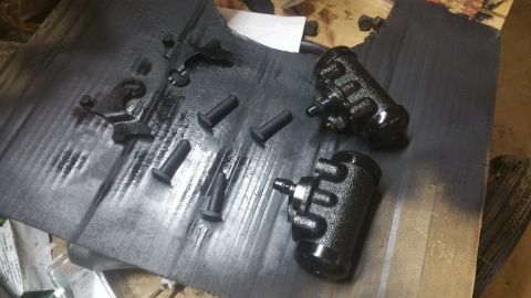 1996 Ford Bronco - Two black brake master cylinders and several black pins are laid out on a black surface with some spray paint residue. Several small black…