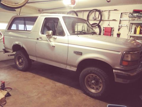 1996 Ford Bronco - A silver Ford Bronco is parked in a garage with various items stored on shelves in the background. The vehicle is viewed from the side, sho…