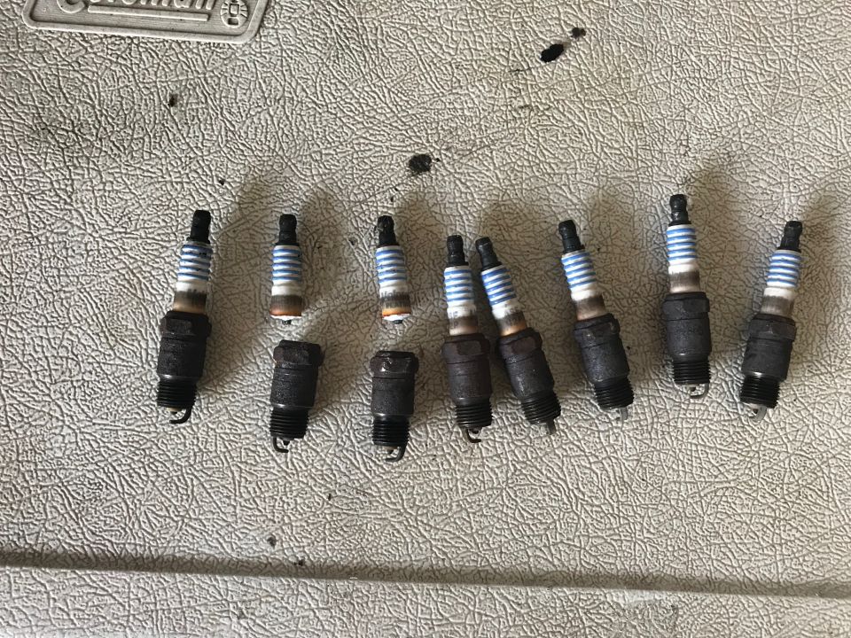 Ten used spark plugs on a textured surface.