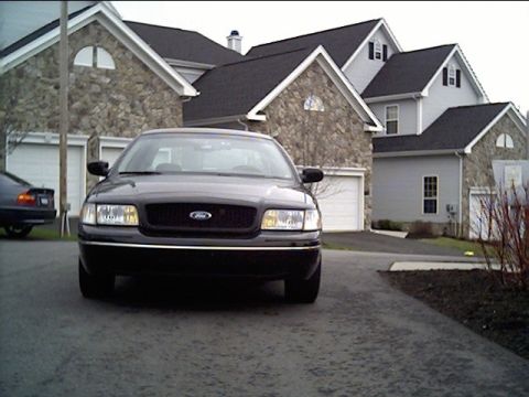 1999 Ford Crown Victoria - Black Ford Crown Victoria parked in front of suburban houses. Another vehicle is partially visible on the left.