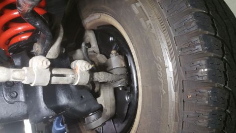 1996 Ford Bronco - A close-up view of the front suspension and steering components of a vehicle, including a red coil spring, tie rod ends, and a tire with vi…