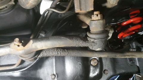 1996 Ford Bronco - This close-up view shows the underside of a vehicle's suspension system, featuring a tie rod end, ball joint, and a red coil spring.